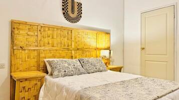 Una habitación con cama, cabecera de madera, dos mesitas de noche y una puerta.
