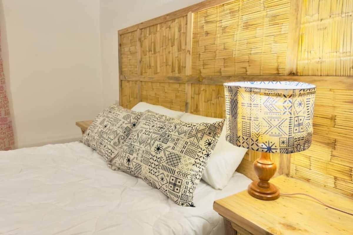 A bed with patterned pillows, a wooden headboard, and a bedside lamp.