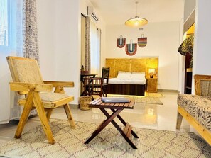 Una habitación con una cama, una silla de madera, una mesita pequeña, una lámpara y una alfombra estampada.