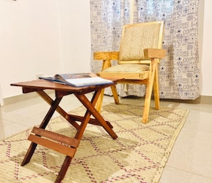 Una silla de madera y una mesita con un libro encima, todo sobre una alfombra estampada.