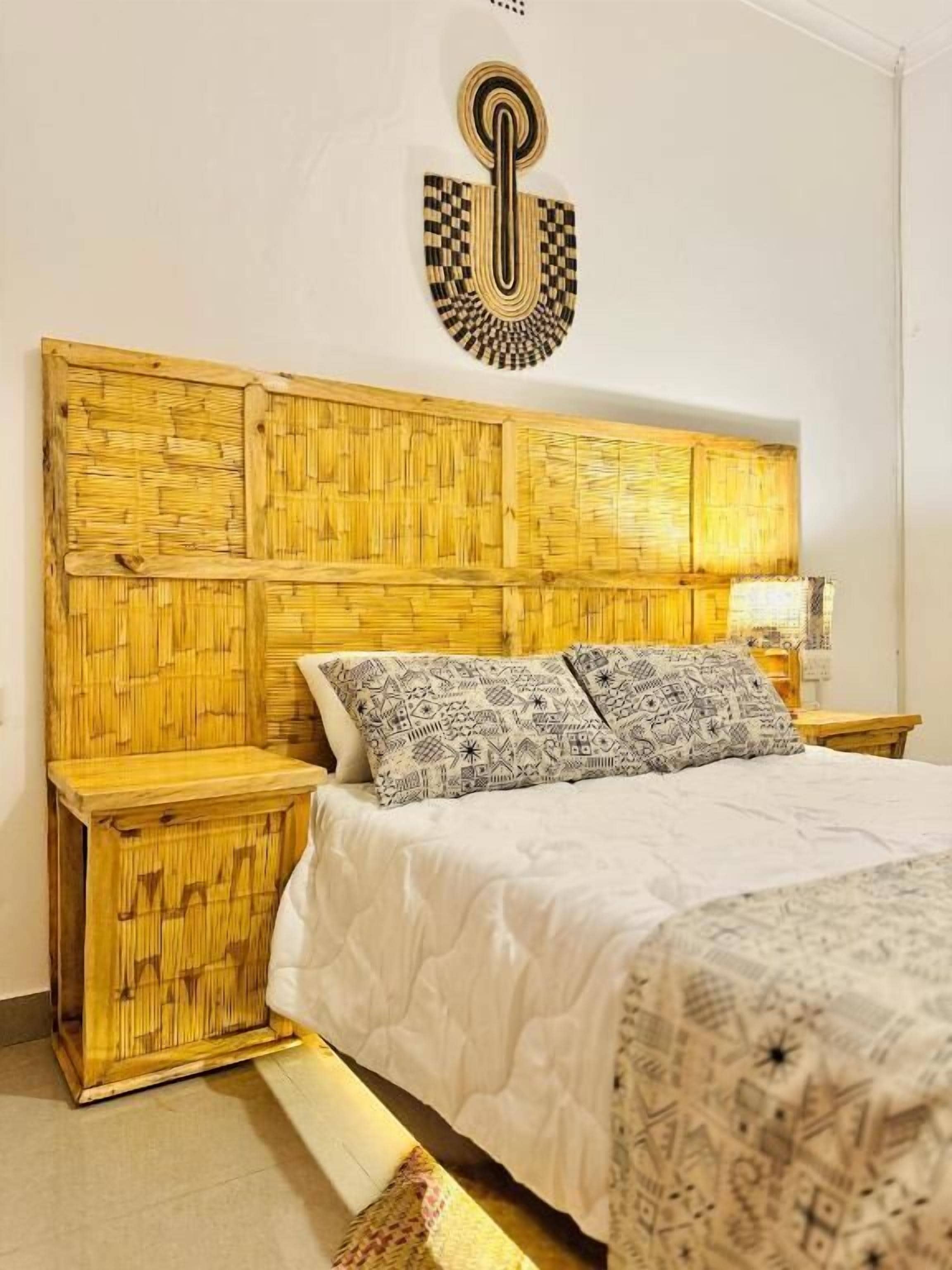 Een kamer met een bed, nachtkastje, een decoratief object aan de muur en een geweven hoofdbord.