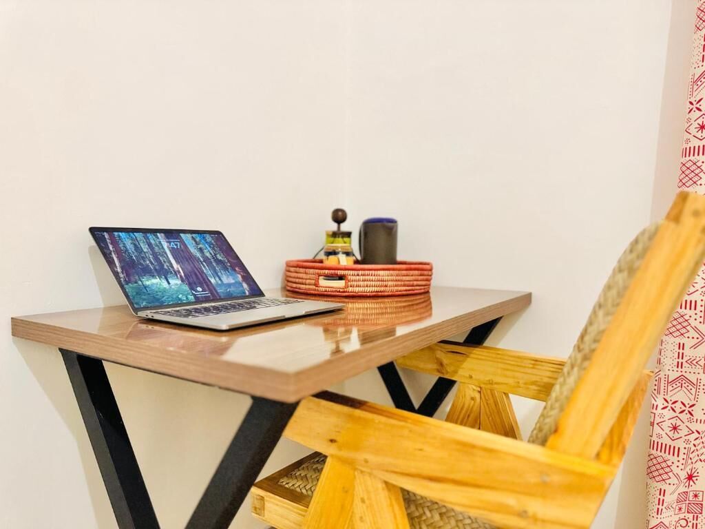 A laptop on a wooden table with a woven basket and a mug.