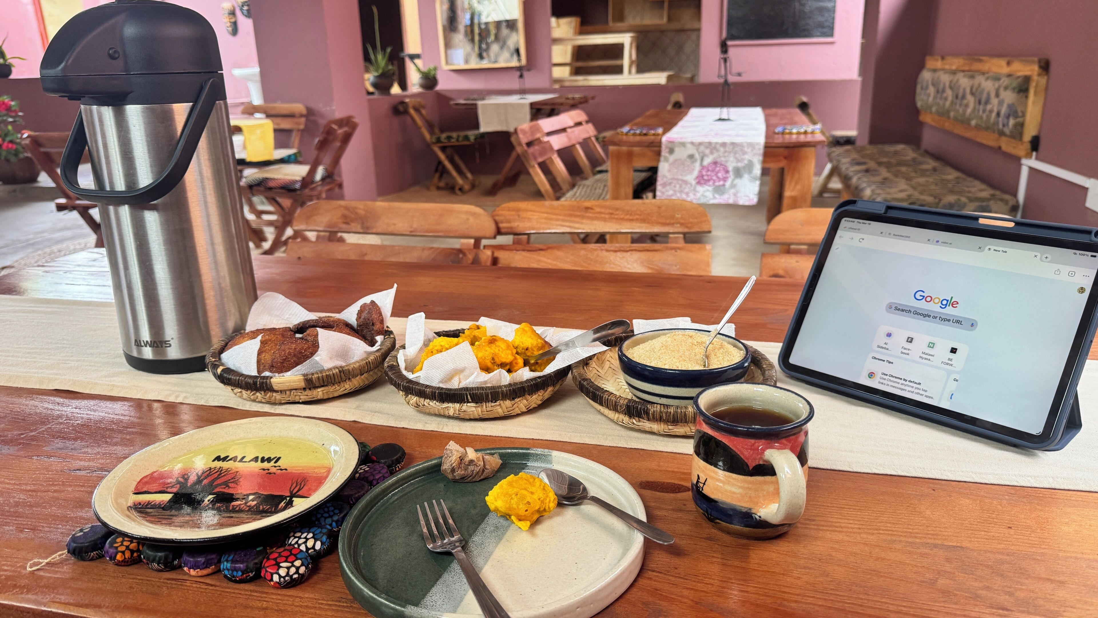 A dining table with a laptop, a thermos, and various dishes including bread, fried snacks, and a bowl of grains.