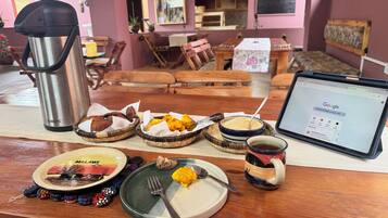 A dining table with a laptop, a thermos, and various dishes including bread, fried snacks, and a bowl of grains.