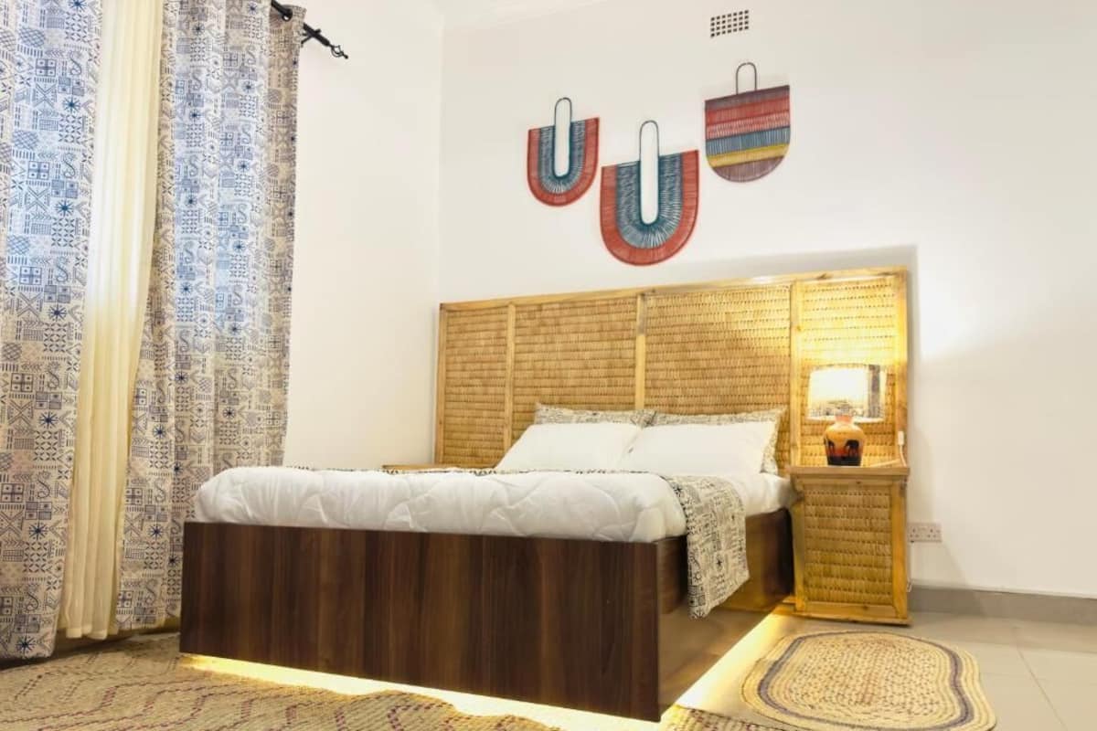 A bedroom with a wooden bed, a bedside table with a lamp, patterned curtains, and wall art.