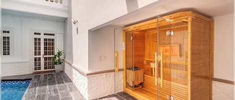 Un espace bien-être comprenant un sauna en bois, une piscine et un mur extérieur blanc.