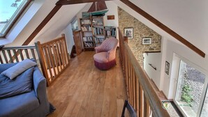 Une pièce de style loft avec des poutres en bois, un mur en pierre, une bibliothèque, un fauteuil violet et un canapé bleu.