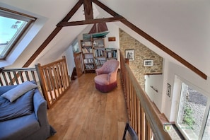 Ein Loft-Zimmer mit Holzbalken, einer Steinwand, einem Bücherregal, einem violetten Sessel und einem blauen Sofa.