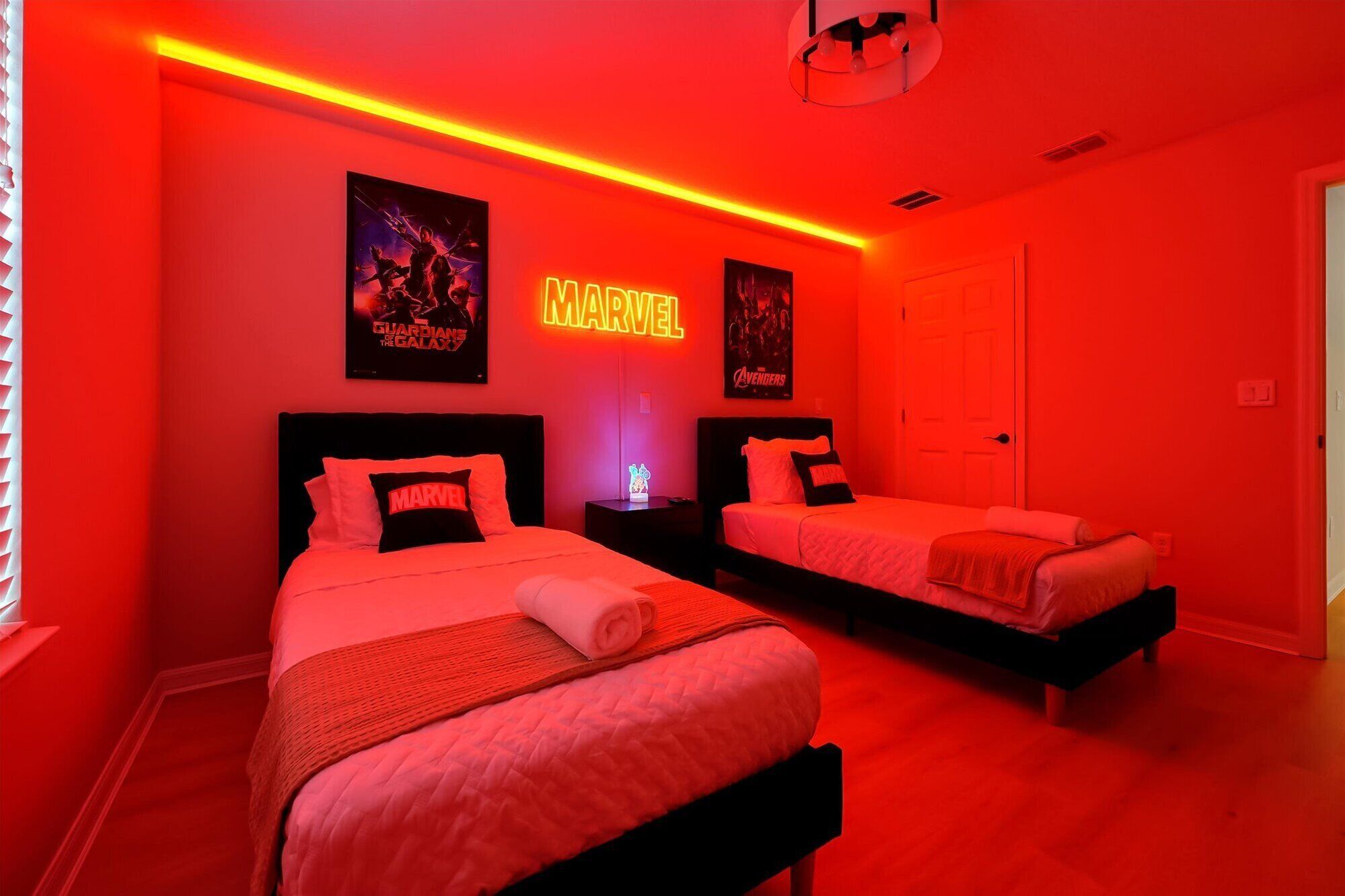 A room with two beds, red walls, and posters of Marvel movies.