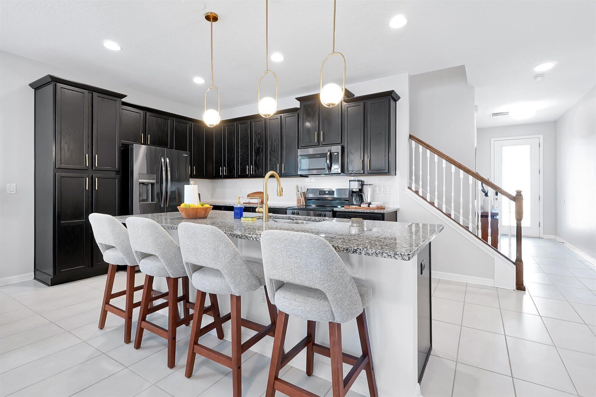 A modern kitchen with dark cabinets, stainless steel appliances, a granite countertop, and a bar stool area.