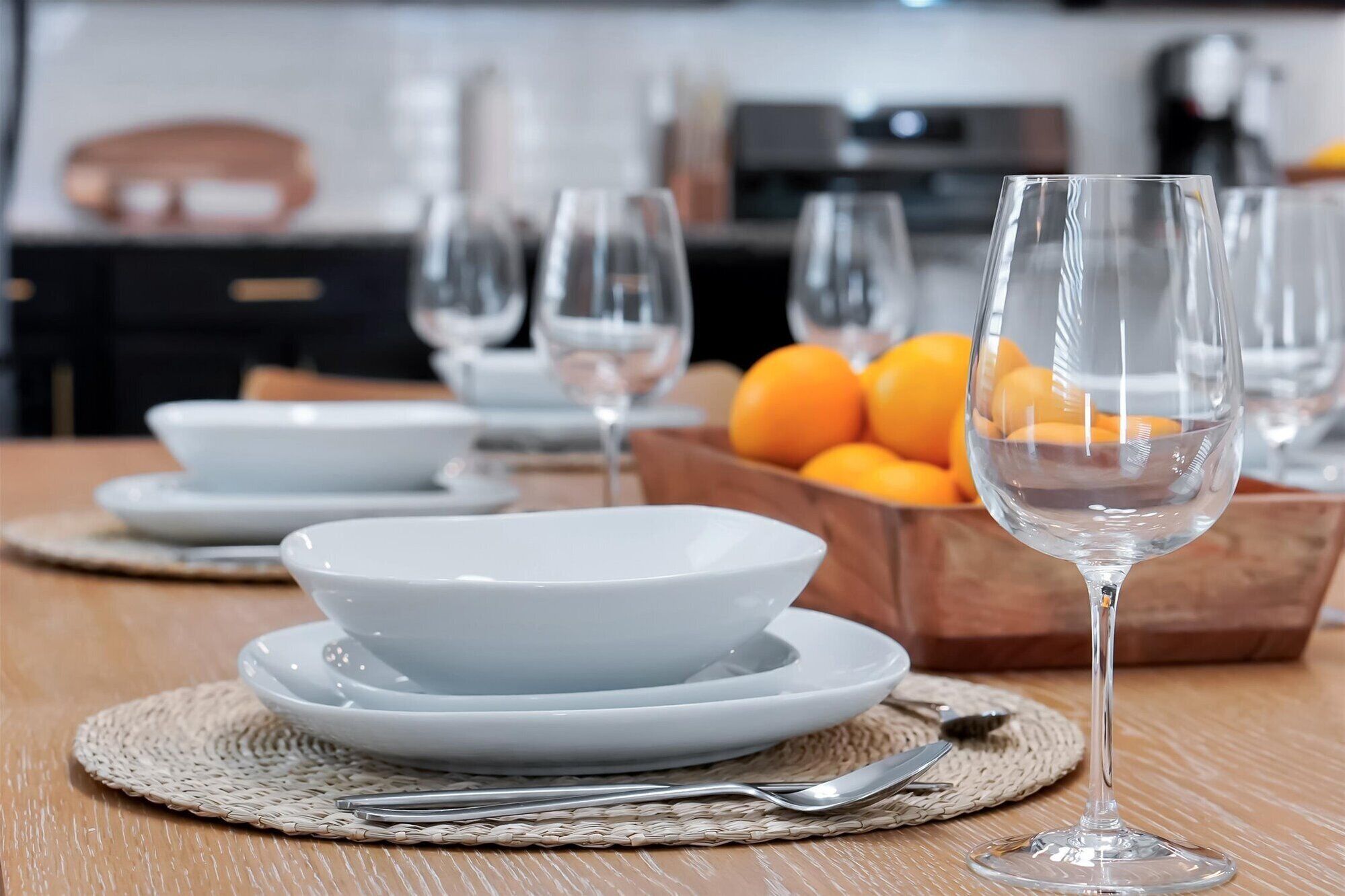 Una mesa de comedor con platos blancos, una copa de vino transparente y un posavasos de mimbre.
