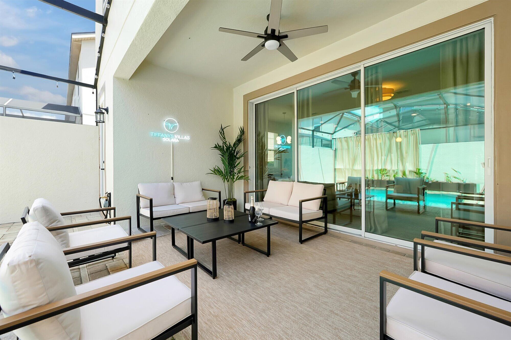 An outdoor seating area with sofas and tables, a ceiling fan, and a glass door leading to an indoor space.