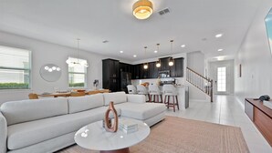 A modern living room with a sofa, a coffee table, and a dining area with chairs and a table. - TIFFANYS VILLAS Solara (Kissimmee)