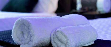 A neatly made white towel on a bed with a dark blue headboard and white bedding.