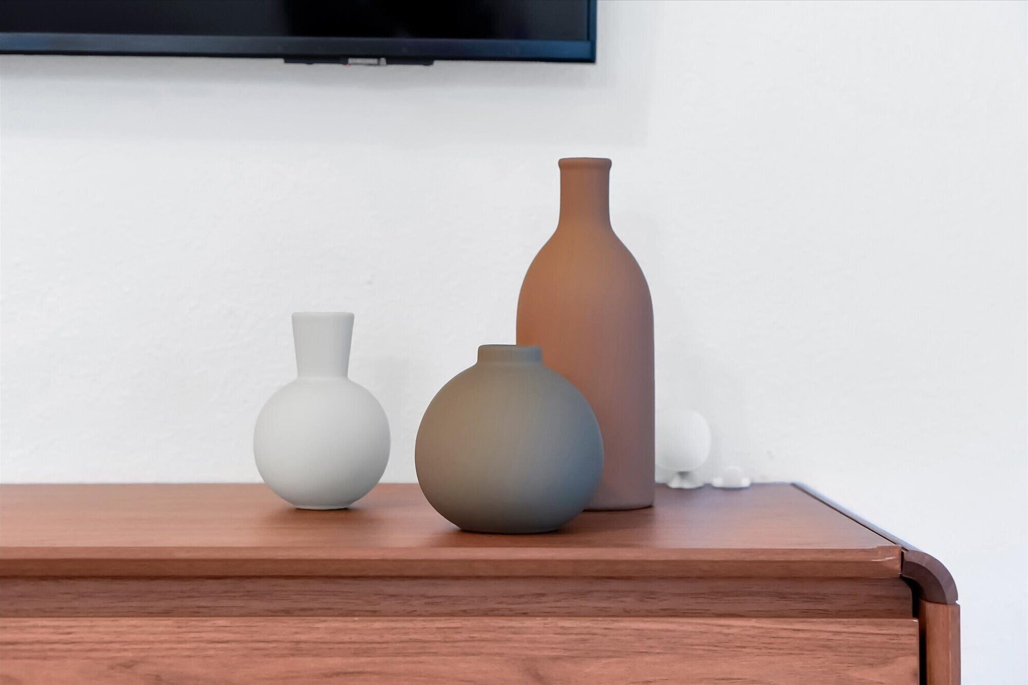 Drie vazen op een houten tafel, tegen een witte muur met een flatscreen televisie erboven.