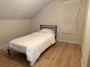 A small, single-bed room with a sloped ceiling, wooden flooring, and a plain white wall. - 2 Queen Beds, 6 Twin beds in Buffalo, NY, University Heights with AC. (Buffalo)
