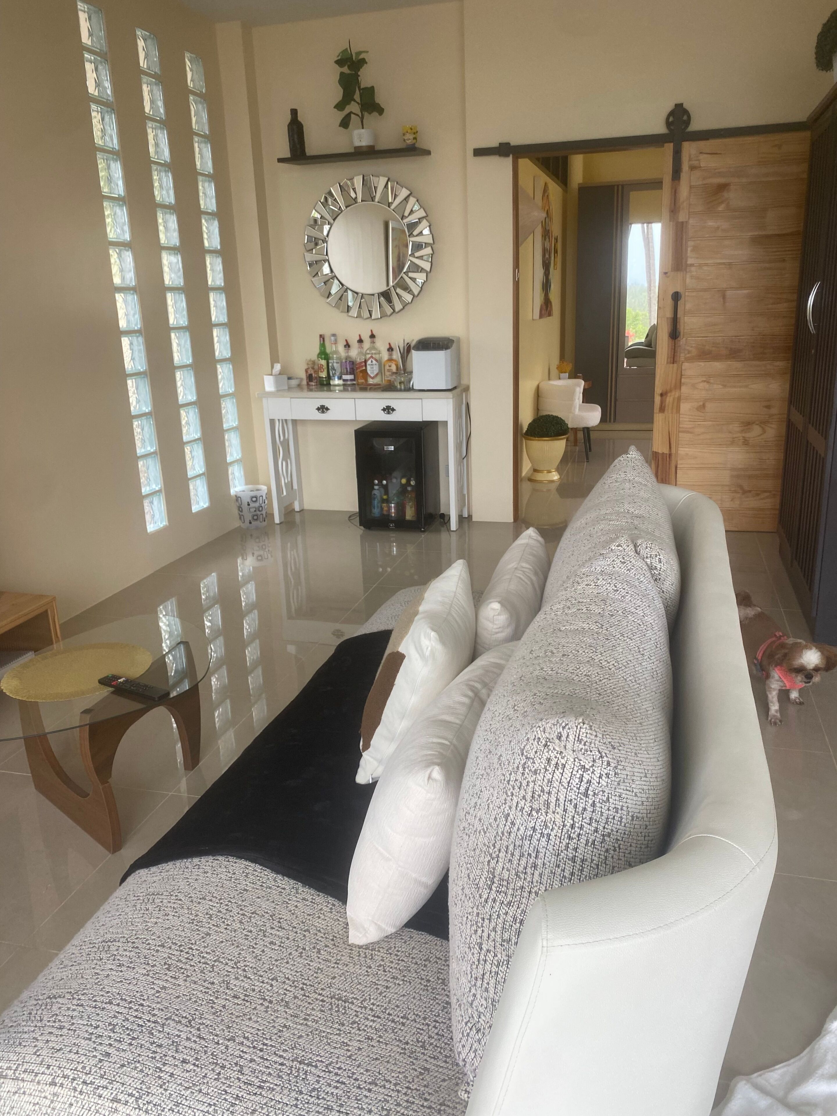 Ein modernes Wohnzimmer mit Sofa, Couchtisch, Glastisch, einer Spiegelwand und einer Tür zu einem weiteren Raum.