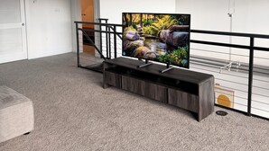 Un'ampia stanza con una grande TV a schermo piatto, una scala e un soffitto in cemento.