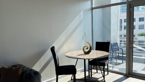 Una camera moderna con un divano, un tavolino rotondo e sedie, ampie finestre con vista sugli edifici e condotti a vista sul soffitto.