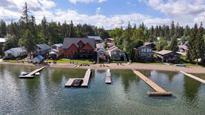Ejendom ved søen med fortøjede både, et hus med terrasse og skov i baggrunden.
