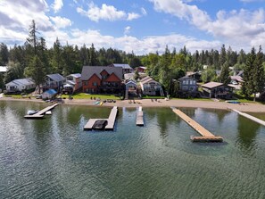 A lakeside property with docked boats, a house with a deck, and a forested backdrop. - Little Hamptons on The Lake (Newport)