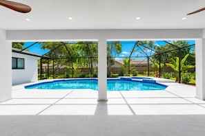 Ein moderner Pool mit klarem, blauem Wasser, umgeben von einer weißen Fliesenveranda und einem Metallzaun.