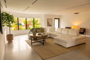 A modern living room with a sectional sofa, a round coffee table, and a large window offering a view of the outdoors. - Coral Springs Oasis Retreat (Coral Springs)