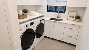 Ein moderner Waschbereich mit einer Waschmaschine und einem Trockner mit Frontlader, einem Spülbecken und einem Fenster mit Jalousien.