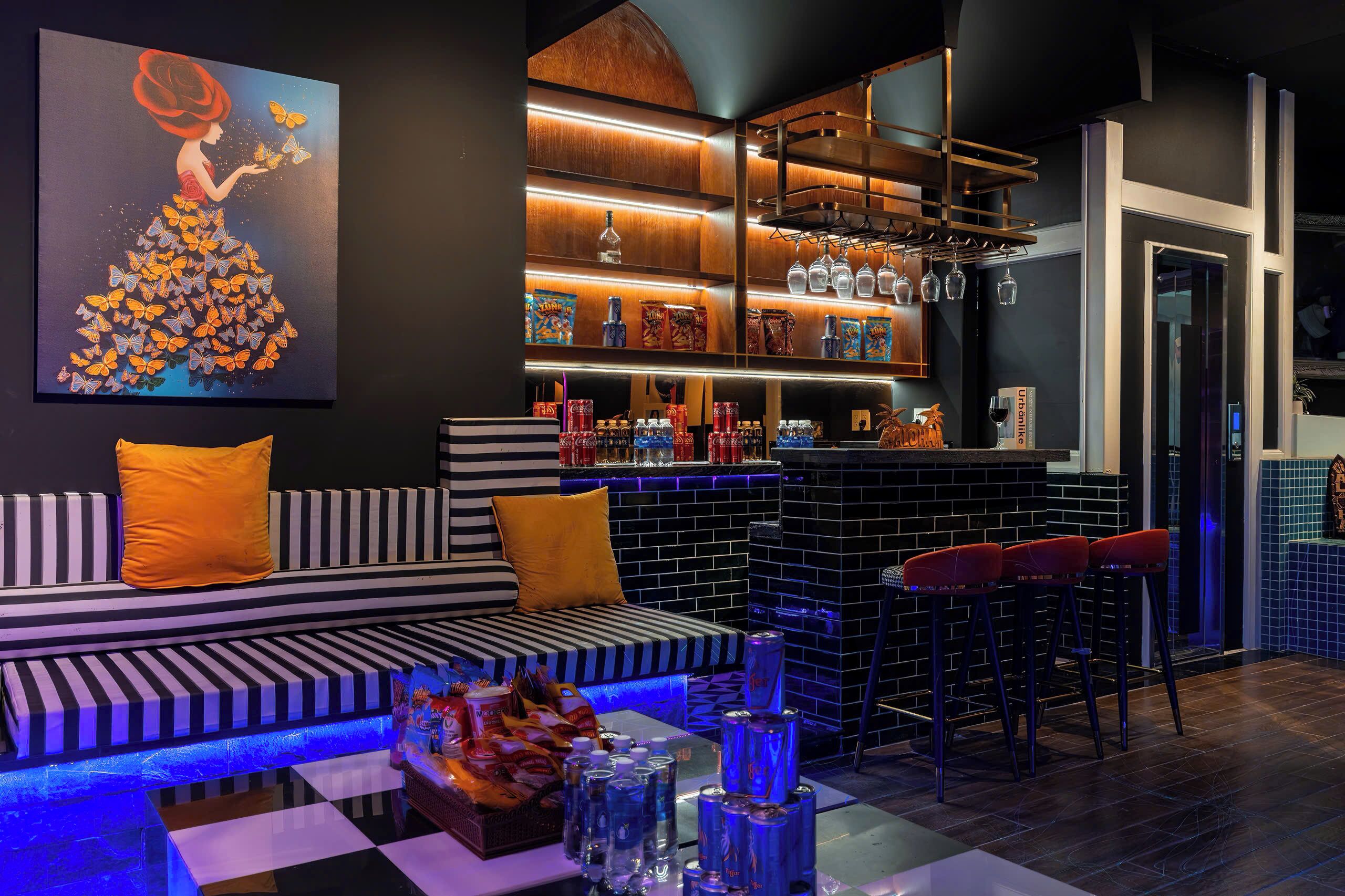 A modern bar area with a black and white striped sofa, a bar counter with stools, and a large painting of a woman surrounded by butterflies.
