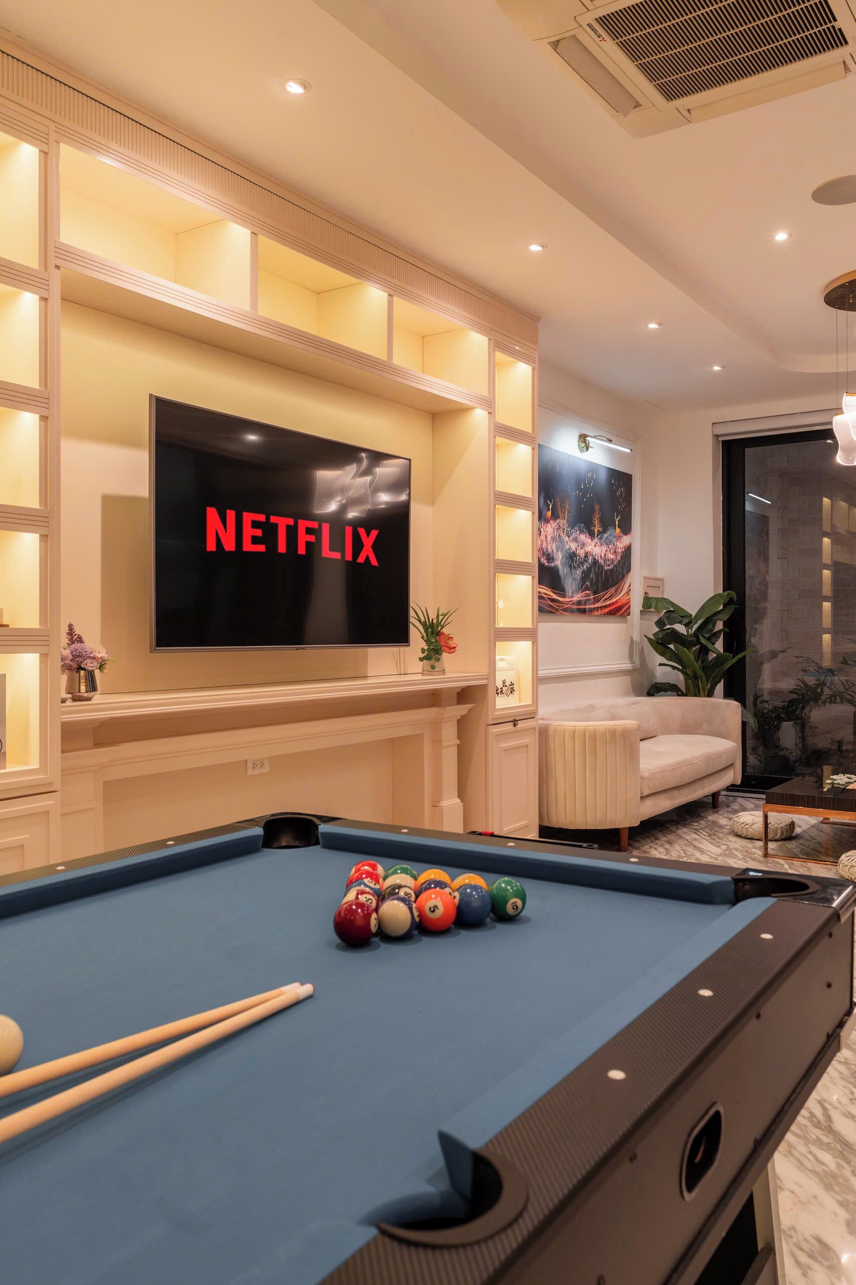 A pool table with balls, a television displaying 'NETFLIX,' and a sofa in a room with a fireplace.