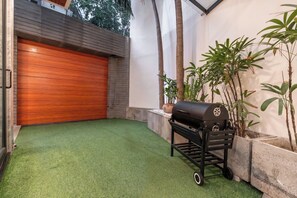 A modern outdoor patio with artificial grass, a barbecue grill, and a wooden garage door. - Tropical Pool Villa D1 with 5 bedrooms (Tan Dinh)