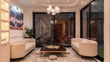 A modern living room with a marble floor, a coffee table, two sofas, a large painting, and a glass door leading to another room.