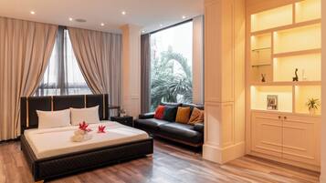 A modern hotel room with a large bed, a sofa, a nightstand, and a built-in shelf with decorative items.