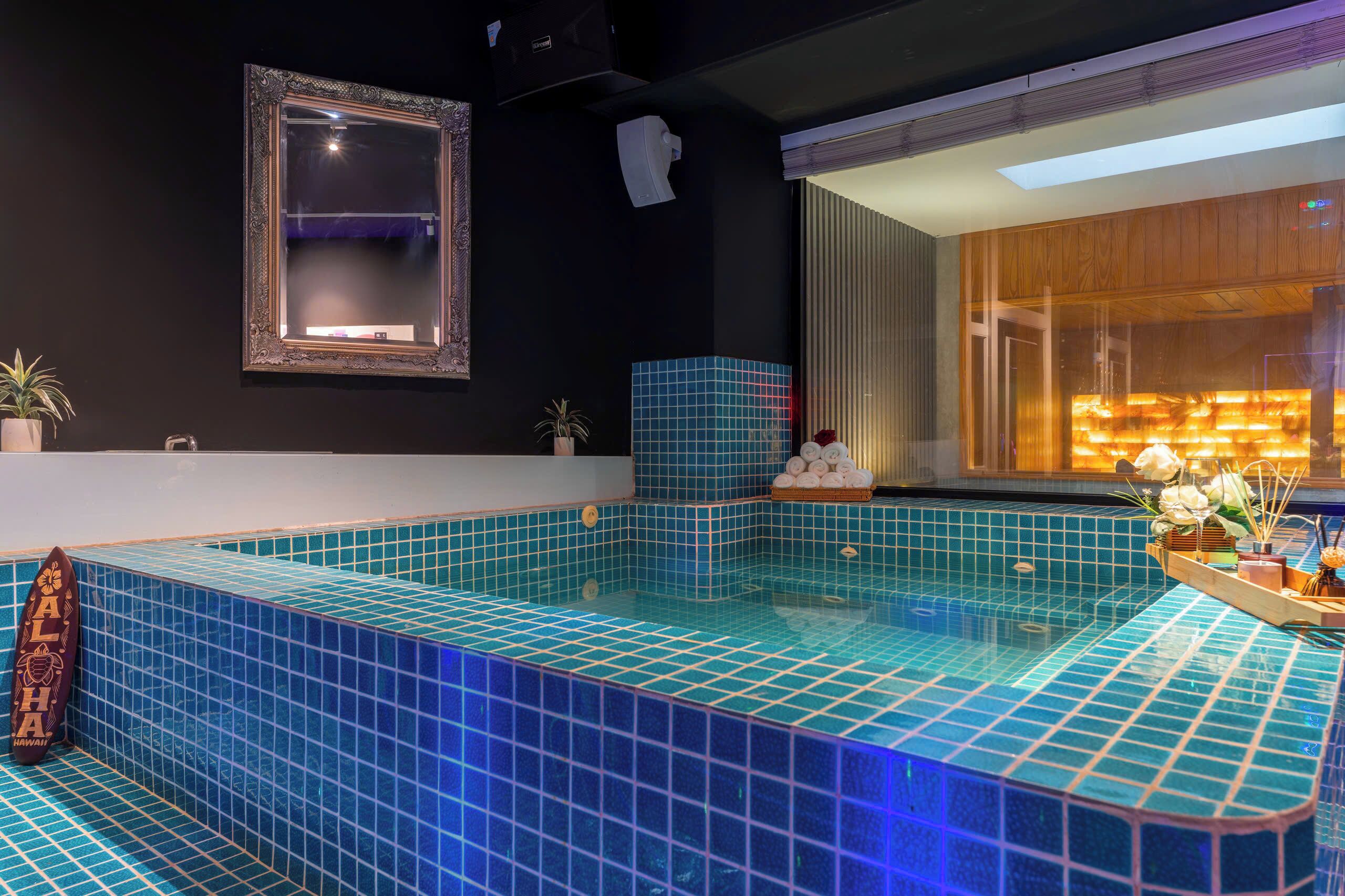 Une piscine intérieure moderne, avec des carreaux bleus, un miroir encadré et un meuble en bois dont l’intérieur est éclairé.