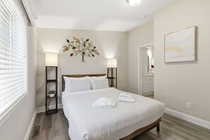 Ein Schlafzimmer mit einem Bett, Nachttischlampen, einem Wandbild und einer Tür zu einem Badezimmer.