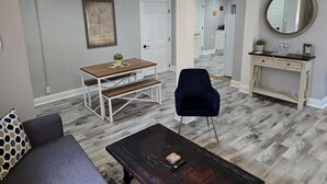 A modern living room with a dining table, a dark blue armchair, a wooden coffee table, and a white console table with a mirror.