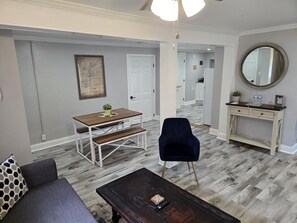 A modern living room with a dining table, a dark blue armchair, a wooden coffee table, and a white console table with a mirror.