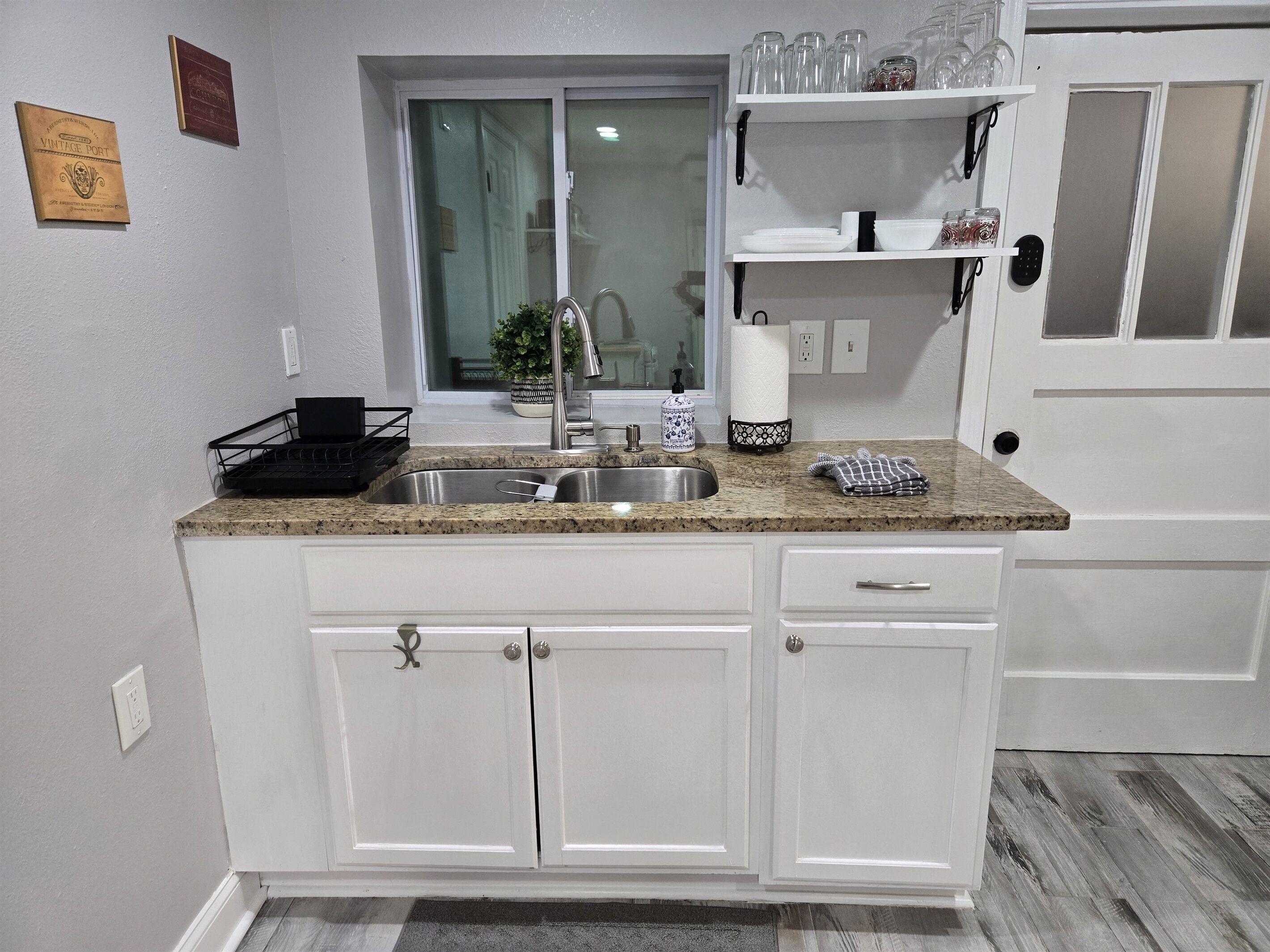 Una cocina con encimera de granito, pileta de acero inoxidable, muebles blancos y ventana con vista.