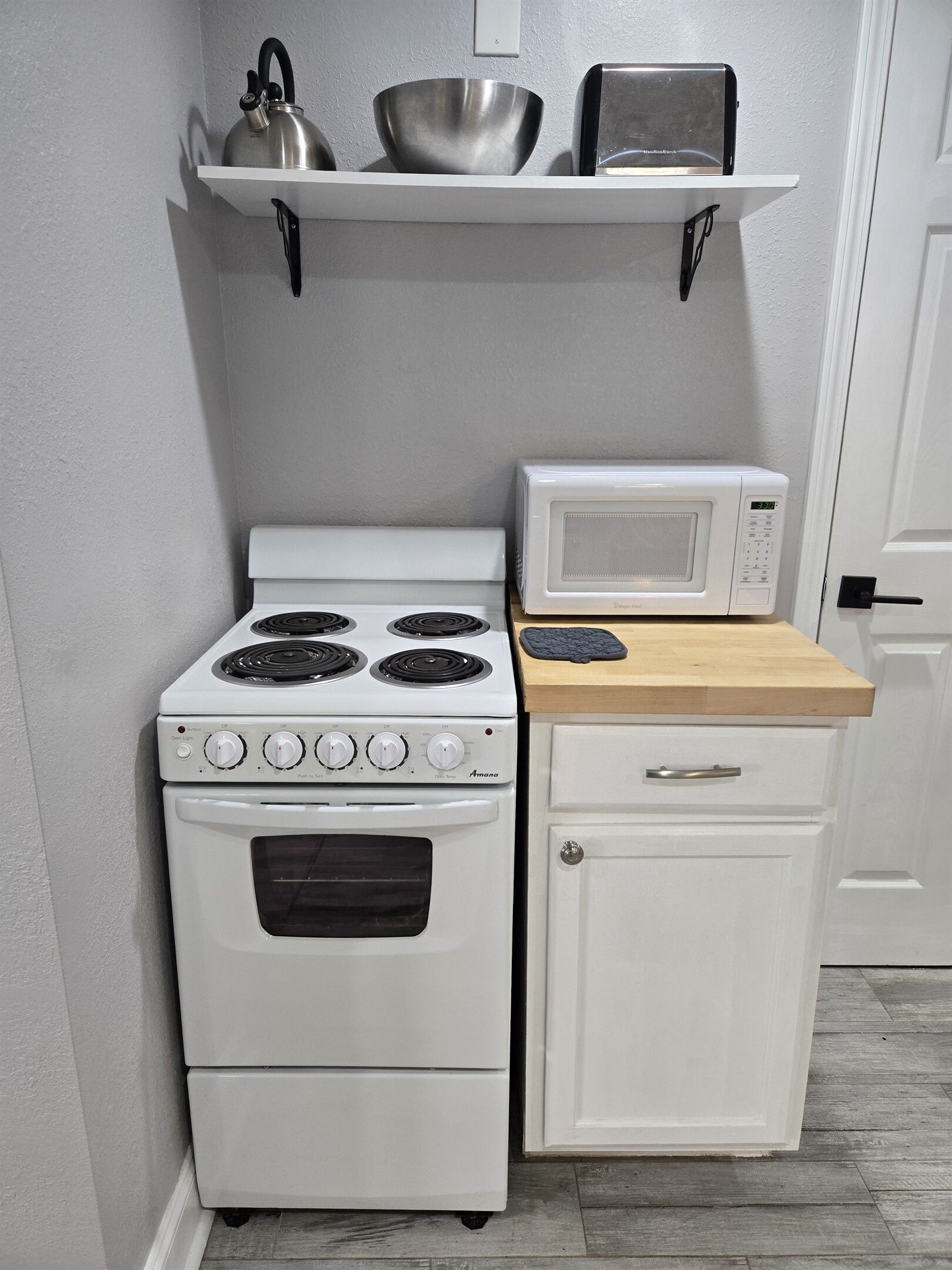 Cozinha compacta com fogão branco, micro-ondas e um armário pequeno.