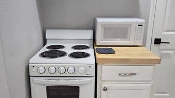 Cozinha compacta com fogão branco, micro-ondas e um armário pequeno.