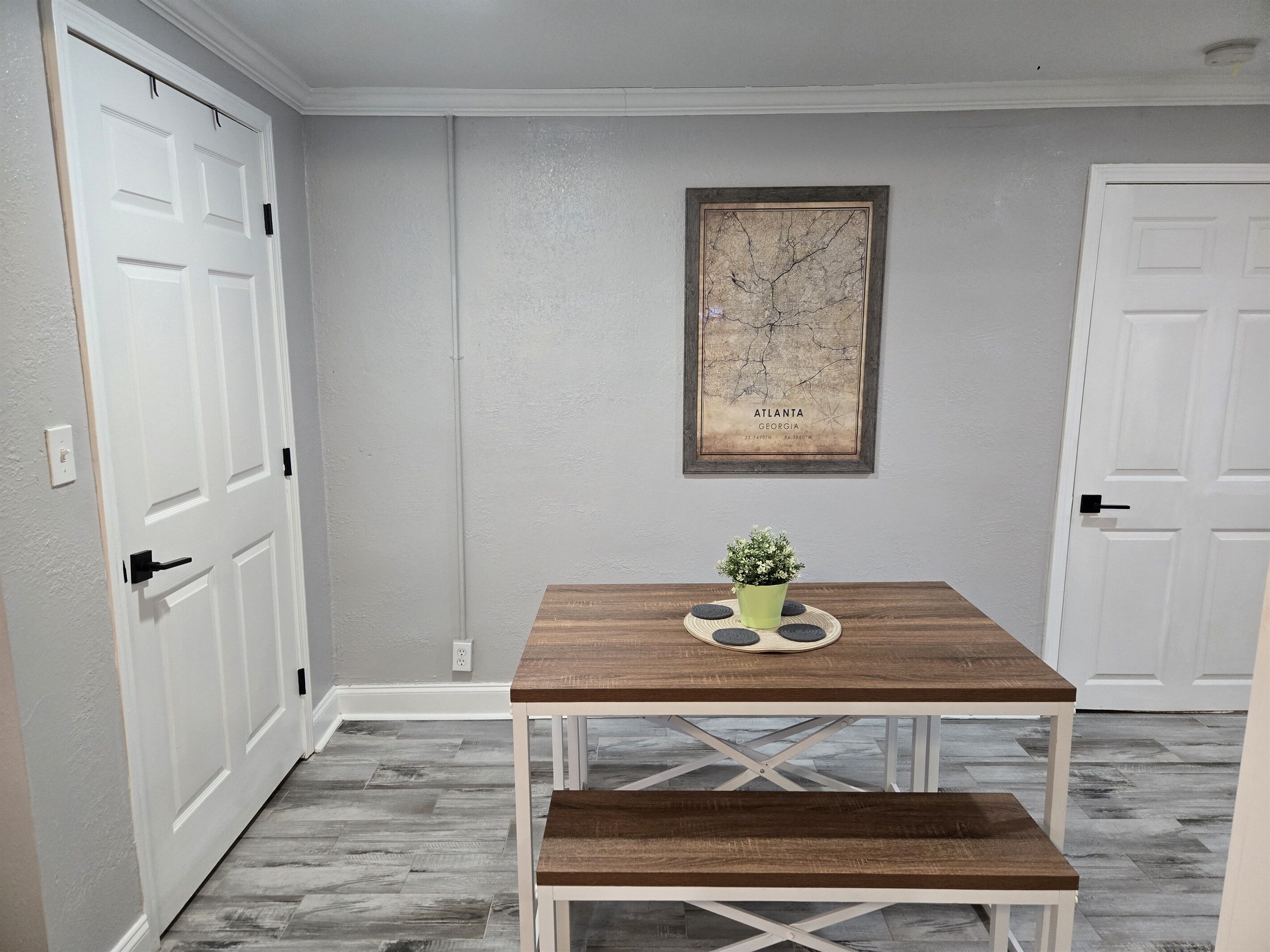 A dining area with a wooden table and bench, a framed map on the wall, and white doors.