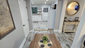 A dining area with a wooden table, a potted plant, and a view into the kitchen.