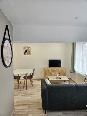 A modern living room with a sofa, a dining table with chairs, a TV on a wooden cabinet, and a framed picture on the wall. - Studio Cosy Centre Valenciennes Station and streetcar on foot (Valenciennes)