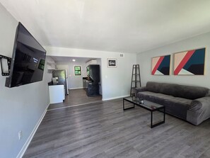 A modern living room with a flat-screen TV, a gray sofa, and abstract wall art. - Gateway City Getaway (Forest Park)