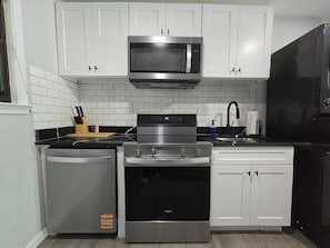 A kitchen with white cabinets, a stainless steel microwave, a stove, and a dishwasher. - Gateway City Getaway (Forest Park)