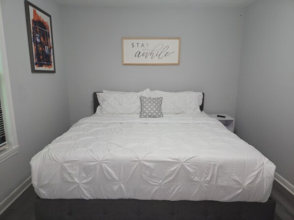 A neatly made bed with a quilted white duvet, a pillow with a geometric pattern, and a framed inspirational quote on the wall. - Gateway City Getaway (Forest Park)