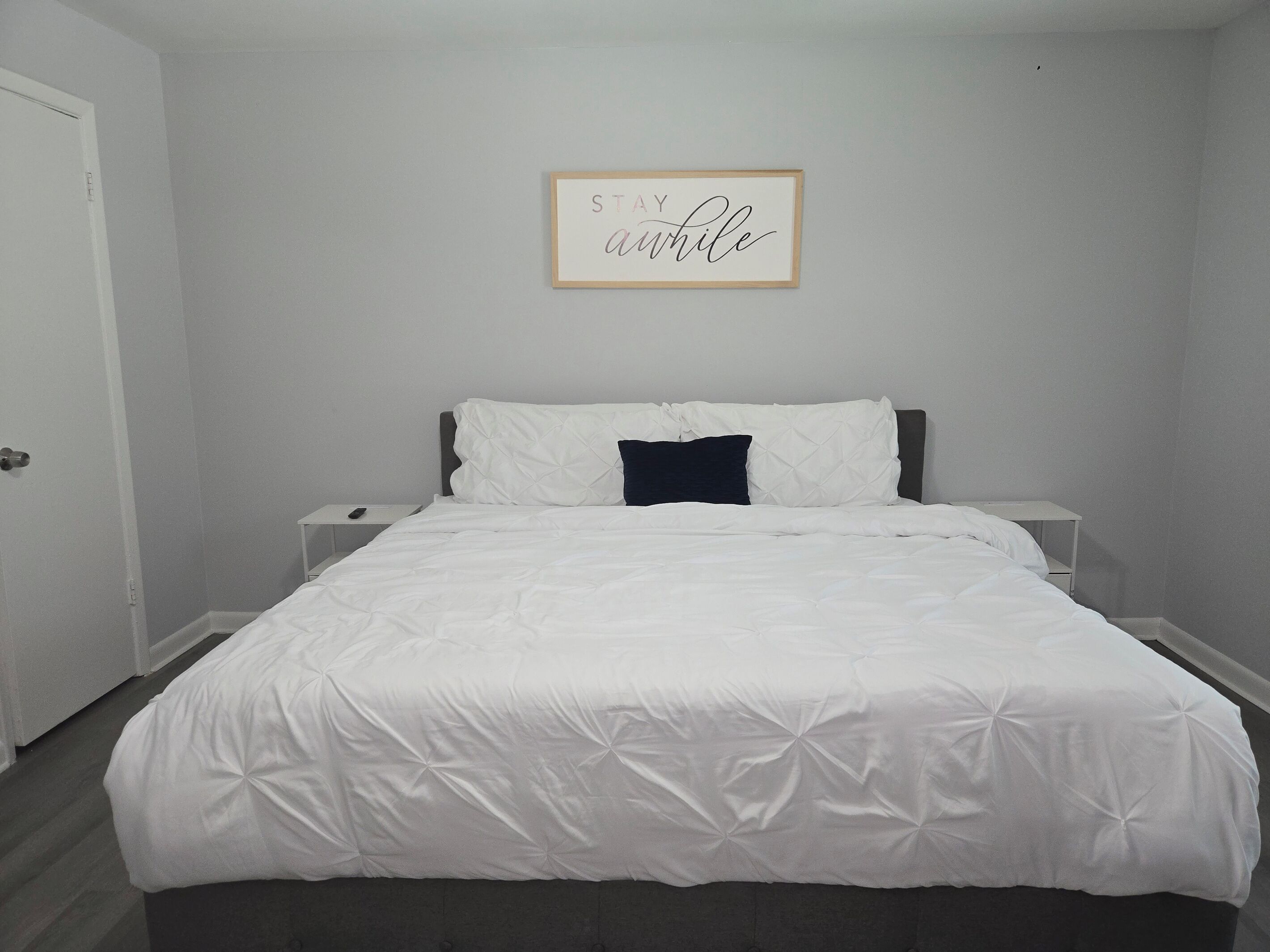 Een slaapkamer met een bed, nachtkastje, raamdecoratie en een deur.