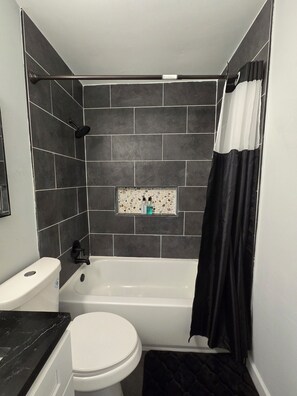 A bathroom with a bathtub, toilet, and shower curtain. - Gateway City Getaway (Forest Park)