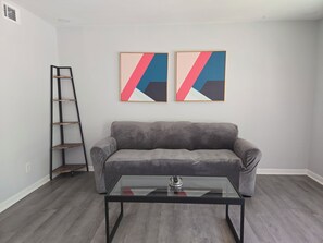 A living room with a gray sofa, a glass coffee table, and two abstract paintings on the wall. - Gateway City Getaway (Forest Park)