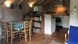 A cozy attic room with a dining table, chairs, a bookshelf, a kitchen area, and a blue chair.